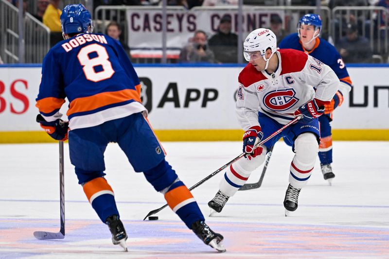 Apr 11, 2024; Elmont, New York, USA; Montreal Canadiens center Nick Suzuki (14) skates the puck across center ice defended by New York Islanders defenseman Noah Dobson (8) during the first period at UBS Arena. Mandatory Credit: Dennis Schneidler-USA TODAY Sports