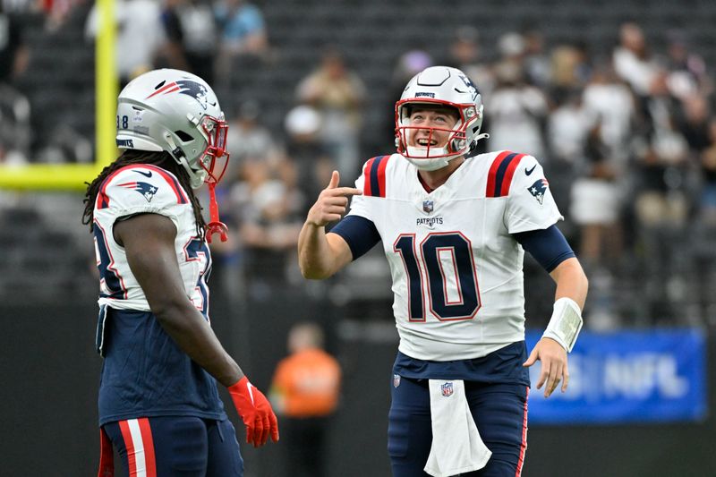 New England Patriots quarterback Mac Jones, right, talks with running back Rhamondre Stevenson before an NFL football game against the Las Vegas Raiders, Sunday, Oct. 15, 2023, in Las Vegas. (AP Photo/David Becker)