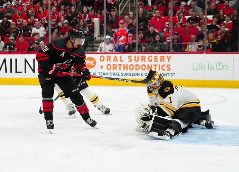 Oct 31, 2024; Raleigh, North Carolina, USA;  Boston Bruins goaltender Jeremy Swayman (1) blocks a shot by Carolina Hurricanes center Sebastian Aho (20) during the first period at Lenovo Center. Mandatory Credit: James Guillory-Imagn Images