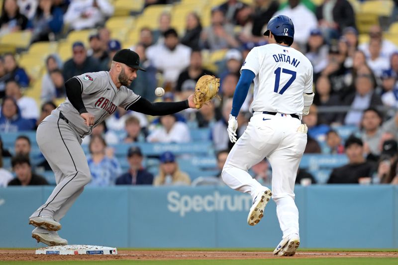 May 20, 2024; Los Angeles, California, USA;  Los Angeles Dodgers designated hitter Shohei Ohtani (17) singles on a bunt as the throw gets past Arizona Diamondbacks first baseman Christian Walker (53) in the first inning at Dodger Stadium. Mandatory Credit: Jayne Kamin-Oncea-USA TODAY Sports