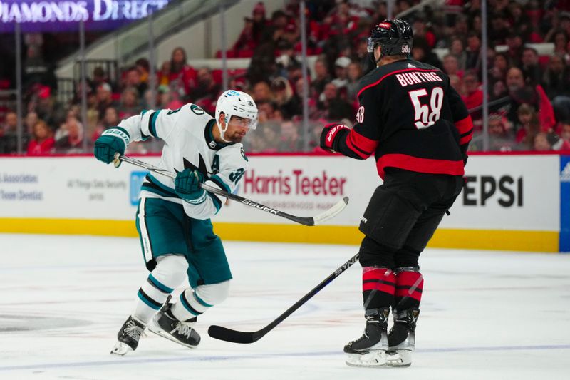 Oct 27, 2023; Raleigh, North Carolina, USA; San Jose Sharks defenseman Mario Ferraro (38) gets the shot off against Carolina Hurricanes left wing Michael Bunting (58) during the second period at PNC Arena. Mandatory Credit: James Guillory-USA TODAY Sports