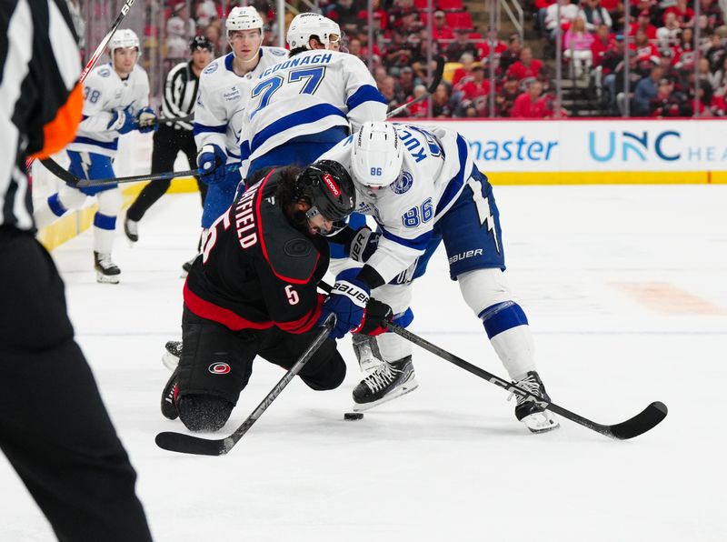 Oct 11, 2024; Raleigh, North Carolina, USA;  Carolina Hurricanes defenseman Jalen Chatfield (5) and Tampa Bay Lightning right wing Nikita Kucherov (86) battle over the puck during the first period at PNC Arena. Mandatory Credit: James Guillory-Imagn Images