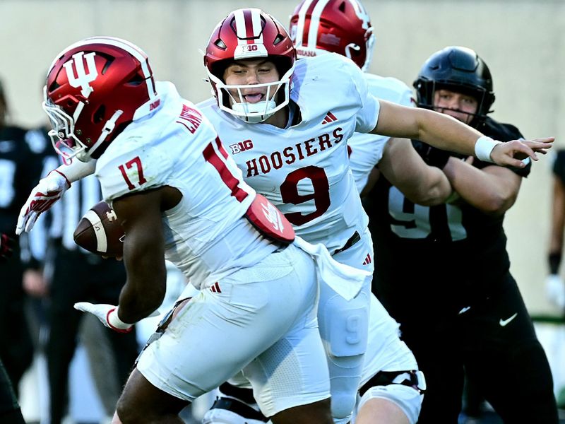 Nov 2, 2024; East Lansing, Michigan, USA;  Indiana Hoosiers quarterback Kurtis Rourke (9) hands the ball to Indiana Hoosiers running back Ty Son Lawton (17) during the third quarter against the Michigan State Spartans at Spartan Stadium. Mandatory Credit: Dale Young-Imagn Images