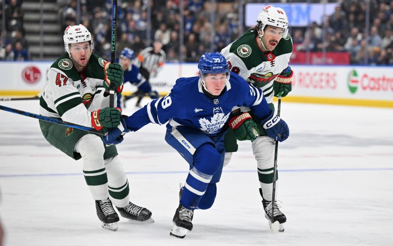 Jan 29, 2025; Toronto, Ontario, CAN;  Toronto Maple Leafs forward Fraser Minten (39) tries to skate past Minnesota Wild defensemen Jake Middleton (5) and Declan Chisholm (47) in the first period at Scotiabank Arena. Mandatory Credit: Dan Hamilton-Imagn Images