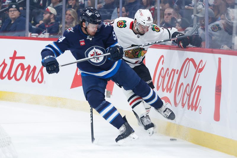 Oct 11, 2024; Winnipeg, Manitoba, CAN;  Winnipeg Jets defenseman Dylan Samberg (54) checks Chicago Blackhawks forward Jason Dickinson (16) during the first period at Canada Life Centre. Mandatory Credit: Terrence Lee-Imagn Images