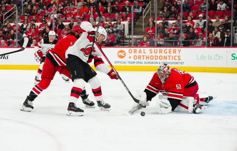 Oct 15, 2024; Raleigh, North Carolina, USA;  Carolina Hurricanes goaltender Pyotr Kochetkov (52) and defenseman Jalen Chatfield (5) stop the scoring attempt by New Jersey Devils left wing Jesper Bratt (63) during the second period at PNC Arena. Mandatory Credit: James Guillory-Imagn Images