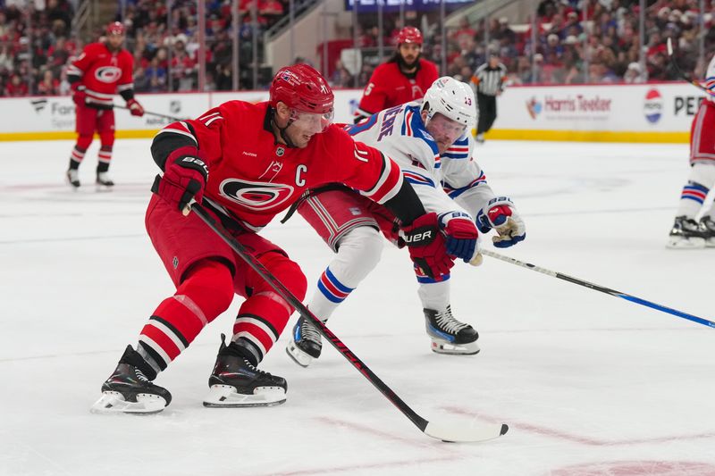 Dec 29, 2025; Raleigh, North Carolina, USA;  Carolina Hurricanes center Jordan Staal (11) skates with the puck outside of New York Rangers left wing Alexis Lafrenière (13) during the third period at Lenovo Center. Mandatory Credit: James Guillory-Imagn Images