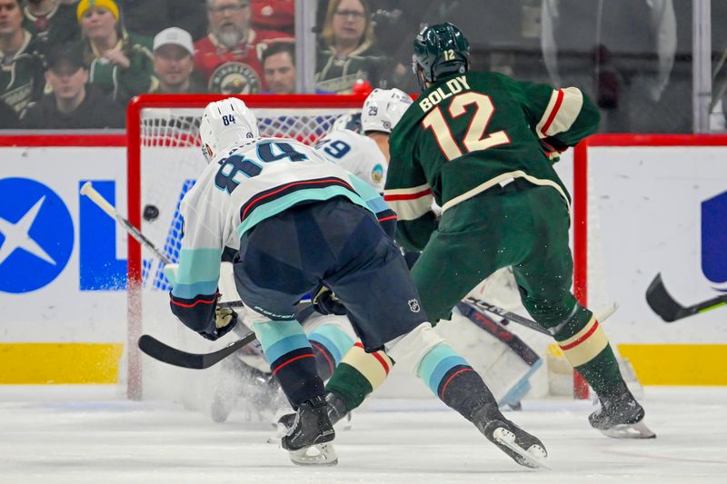 Mar 19, 2025; Saint Paul, Minnesota, USA;  Minnesota Wild forward Matt Boldy (12) scores a goal as Seattle Kraken forward Kaapo Kakko (84) defends during the first period at Xcel Energy Center. Mandatory Credit: Nick Wosika-Imagn Images