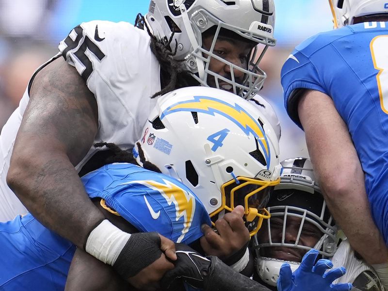 Los Angeles Chargers running back Gus Edwards (4) is tackled by Las Vegas Raiders defensive tackle John Jenkins, top, and linebacker Divine Deablo during the first half of an NFL football game, Sunday, Sept. 8, 2024, in Inglewood, Calif. (AP Photo/Marcio Jose Sanchez)