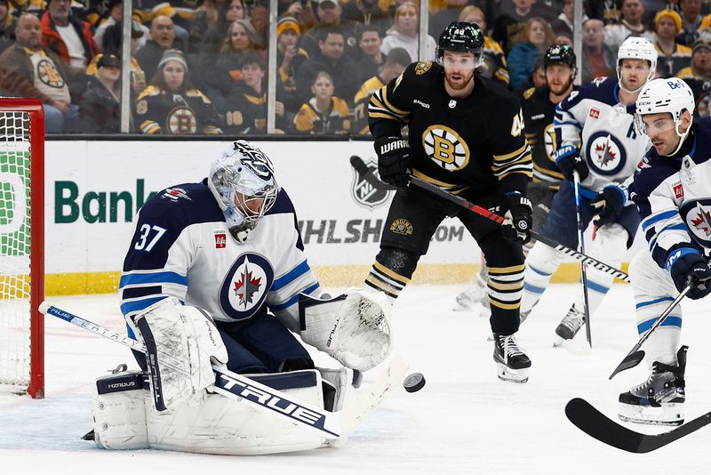 Jan 22, 2024; Boston, Massachusetts, USA; Winnipeg Jets goaltender Connor Hellebuyck (37) eyes a loose puck as Boston Bruins defenseman Matt Grzelcyk (48) moves in during the second period at TD Garden. Mandatory Credit: Winslow Townson-USA TODAY Sports