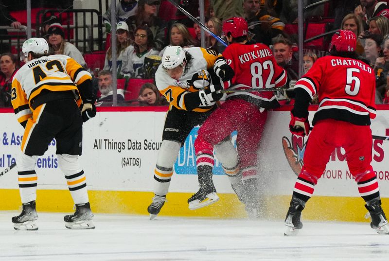 Jan 13, 2024; Raleigh, North Carolina, USA;  Pittsburgh Penguins defenseman Ryan Graves (27) checks Carolina Hurricanes center Jesperi Kotkaniemi (82) during the second period at PNC Arena. Mandatory Credit: James Guillory-USA TODAY Sports