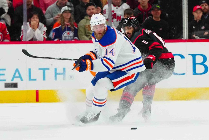 Nov 22, 2023; Raleigh, North Carolina, USA; Edmonton Oilers defenseman Mattias Ekholm (14) tries to control the puck against Carolina Hurricanes defenseman Jalen Chatfield (5) during the first period at PNC Arena. Mandatory Credit: James Guillory-USA TODAY Sports