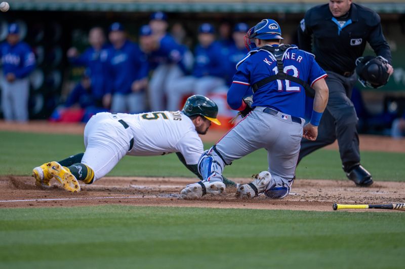 May 6, 2024; Oakland, California, USA; Oakland Athletics first baseman J.D. Davis (5) dives in safely against Texas Rangers catcher Andrew Knizner (12) during the second inning at Oakland-Alameda County Coliseum. Mandatory Credit: Neville E. Guard-USA TODAY Sports