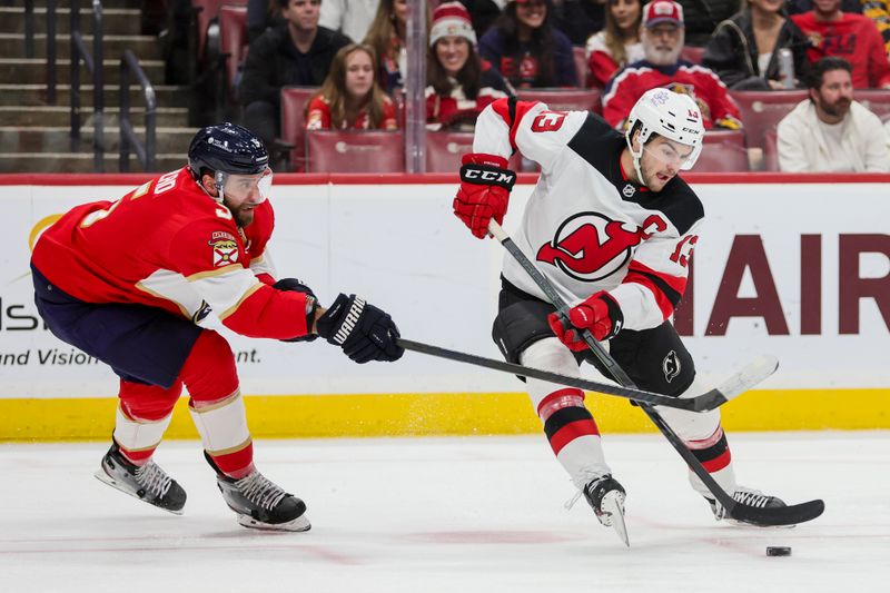 Jan 13, 2024; Sunrise, Florida, USA; New Jersey Devils center Nico Hischier (13) protects the puck from Florida Panthers defenseman Aaron Ekblad (5) during the first period at Amerant Bank Arena. Mandatory Credit: Sam Navarro-USA TODAY Sports