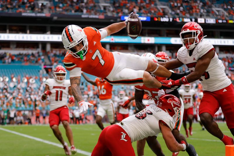 Nov 18, 2023; Miami Gardens, Florida, USA; Miami Hurricanes wide receiver Xavier Restrepo (7) leaps over Louisville Cardinals defensive lineman Mason Reiger (95) for a touchdown during the first quarter at Hard Rock Stadium. Mandatory Credit: Sam Navarro-USA TODAY Sports