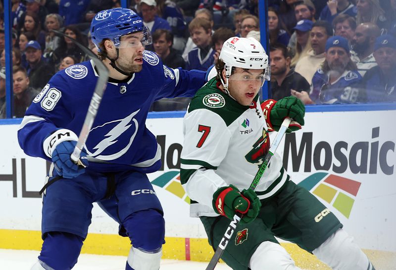 Jan 18, 2024; Tampa, Florida, USA; Tampa Bay Lightning left wing Brandon Hagel (38) ands Minnesota Wild defenseman Brock Faber (7) skate after the puck during the first period at Amalie Arena. Mandatory Credit: Kim Klement Neitzel-USA TODAY Sports