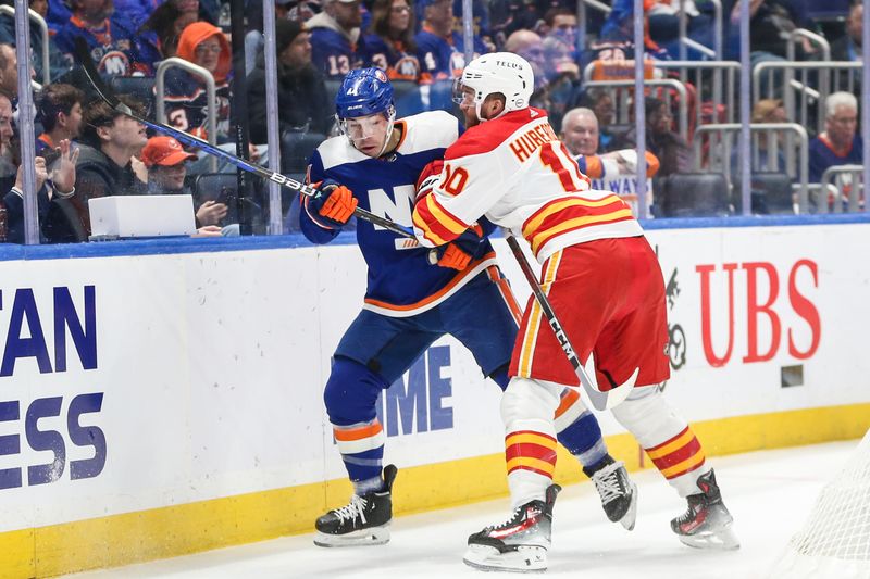 Feb 10, 2024; Elmont, New York, USA;  New York Islanders defenseman Samuel Bolduc (4) and Calgary Flames center Jonathan Huberdeau (10) battle for position in this first period at UBS Arena. Mandatory Credit: Wendell Cruz-USA TODAY Sports 