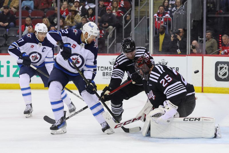 Mar 7, 2025; Newark, New Jersey, USA; New Jersey Devils goaltender Jacob Markstrom (25) makes a save on Winnipeg Jets right wing Nino Niederreiter (62) during the first period at Prudential Center. Mandatory Credit: Ed Mulholland-Imagn Images