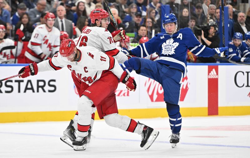 Dec 30, 2023; Toronto, Ontario, CAN; Toronto Maple Leafs forward Mitchell Marner (16) loses his balance after a collision with Carolina Hurricanes forward Jordan Staal (11) and defenseman Brady Skjei (76) in the third period at Scotiabank Arena. Mandatory Credit: Dan Hamilton-USA TODAY Sports