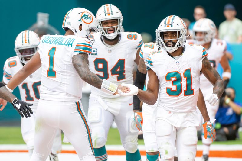 Miami Dolphins running back Raheem Mostert (31) celebrates scoring a touchdown with Miami Dolphins quarterback Tua Tagovailoa (1) during an NFL football game between the against the New England Patriots, Sunday, Oct. 29, 2023, in Miami Gardens, Fla. (AP Photo/Doug Murray)