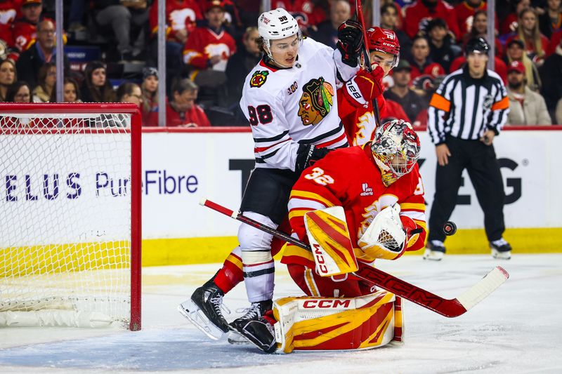 Nov 7, 2025; Calgary, Alberta, CAN; Calgary Flames defenseman Zayne Parekh (19) and Chicago Blackhawks center Connor Bedard (98) battles for the puck as Calgary Flames goaltender Dustin Wolf (32) makes a save during the first period at Scotiabank Saddledome. Mandatory Credit: Sergei Belski-Imagn Images