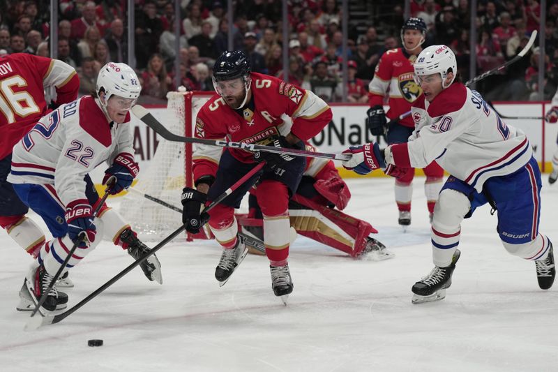 Dec 30, 2023; Sunrise, Florida, USA; Montreal Canadiens right wing Cole Caufield (22) and Florida Panthers defenseman Aaron Ekblad (5) battle for possession as Canadiens left wing Juraj Slafkovsky (20) closes in during the first period at Amerant Bank Arena. Mandatory Credit: Jim Rassol-USA TODAY Sports