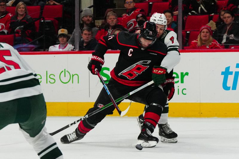 Jan 21, 2024; Raleigh, North Carolina, USA; Carolina Hurricanes center Jordan Staal (11) tries to control the puck against Minnesota Wild defenseman Brock Faber (7) during the first period at PNC Arena. Mandatory Credit: James Guillory-USA TODAY Sports