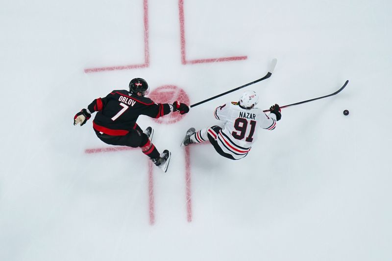 Jan 30, 2025; Raleigh, North Carolina, USA;  Chicago Blackhawks center Frank Nazar (91) skates with the puck against Carolina Hurricanes defenseman Dmitry Orlov (7) during the second period at Lenovo Center. Mandatory Credit: James Guillory-Imagn Images