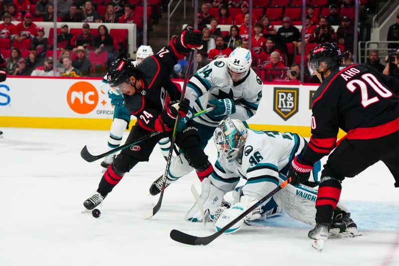 Oct 27, 2023; Raleigh, North Carolina, USA; Carolina Hurricanes center Seth Jarvis (24) battles for the puck against San Jose Sharks goaltender Kaapo Kahkonen (36) and defenseman Jan Rutta (84) during the first period at PNC Arena. Mandatory Credit: James Guillory-USA TODAY Sports