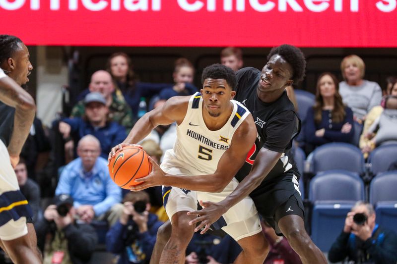 Jan 6, 2026; Morgantown, West Virginia, USA; West Virginia Mountaineers forward DJ Thomas (5) looks to pass while being defended by Cincinnati Bearcats center Moustapha Thiam (52) during the first half at Hope Coliseum. Mandatory Credit: Ben Queen-Imagn Images