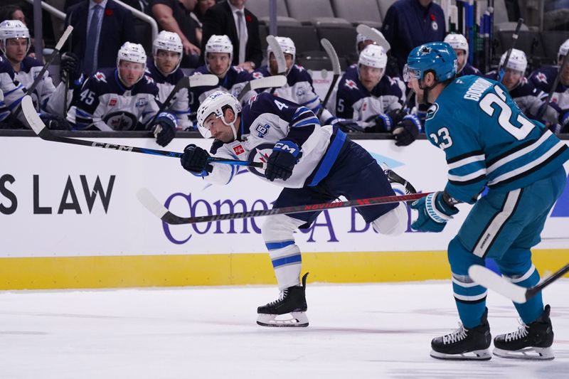 Nov 7, 2025; San Jose, California, USA; Winnipeg Jets defenseman Neal Pionk (4) passes the puck against San Jose Sharks center Barclay Goodrow (23) in the first period at SAP Center at San Jose. Mandatory Credit: David Gonzales-Imagn Images