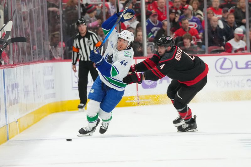 Nov 14, 2025; Raleigh, North Carolina, USA;  Vancouver Canucks left wing Kiefer Sherwood (44) spins away from the check by Carolina Hurricanes defenseman Shayne Gostisbehere (4) during the second period at Lenovo Center. Mandatory Credit: James Guillory-Imagn Images