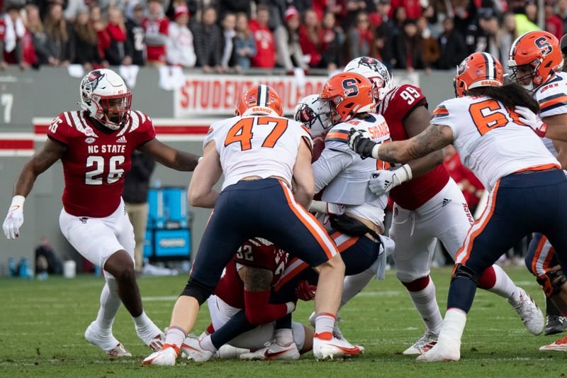 Nov 20, 2021; Raleigh, North Carolina, USA; Syracuse Orange quarterback Garrett Shrader (16) is tackled by North Carolina State Wolfpack linebacker Drake Thomas (32) and defensive lineman Daniel Joseph (99) during the second half at Carter-Finley Stadium. Mandatory Credit: William Howard-USA TODAY Sports