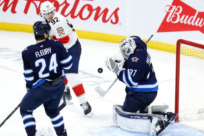 Nov 19, 2024; Winnipeg, Manitoba, CAN; Winnipeg Jets defenseman Haydn Fleury (24) and Florida Panthers left wing Tomas Nosek (92) watch Winnipeg Jets goaltender Connor Hellebuyck (37) stop a shot in the third period  at Canada Life Centre. Mandatory Credit: James Carey Lauder-Imagn Images