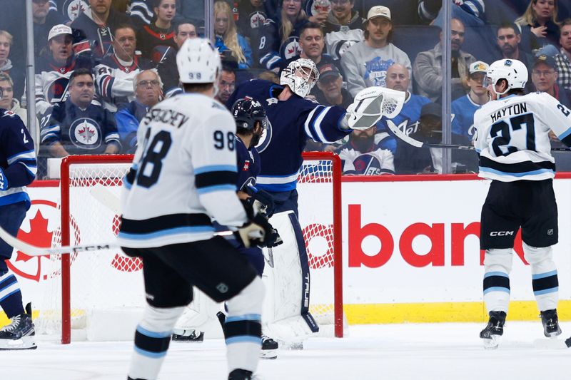 Nov 5, 2024; Winnipeg, Manitoba, CAN;  Winnipeg Jets goalie Connor Hellebuyck (37) catches the puck as Utah Hockey Club forward Barrett Hayton (27) looks for a rebound during the second period at Canada Life Centre. Mandatory Credit: Terrence Lee-Imagn Images