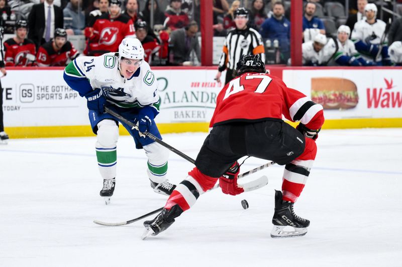 Dec 14, 2025; Newark, New Jersey, USA; Vancouver Canucks defenseman Zeev Buium (24) skates with the puck while defended by New Jersey Devils left wing Paul Cotter (47) during the first period at Prudential Center. Mandatory Credit: John Jones-Imagn Images