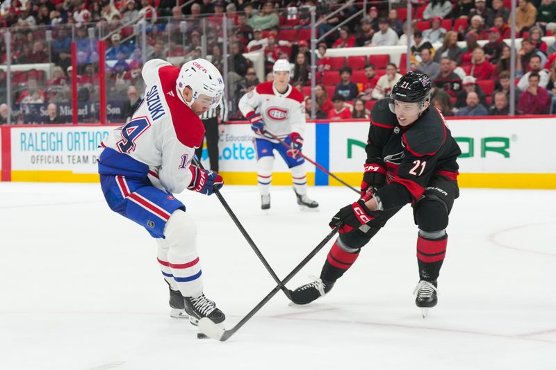 Jan 1, 2026; Raleigh, North Carolina, USA;  Carolina Hurricanes defenseman Alexander Nikishin (21) pokes the puck away from Montréal Canadiens center Nick Suzuki (14) during the second period at Lenovo Center. Mandatory Credit: James Guillory-Imagn Images