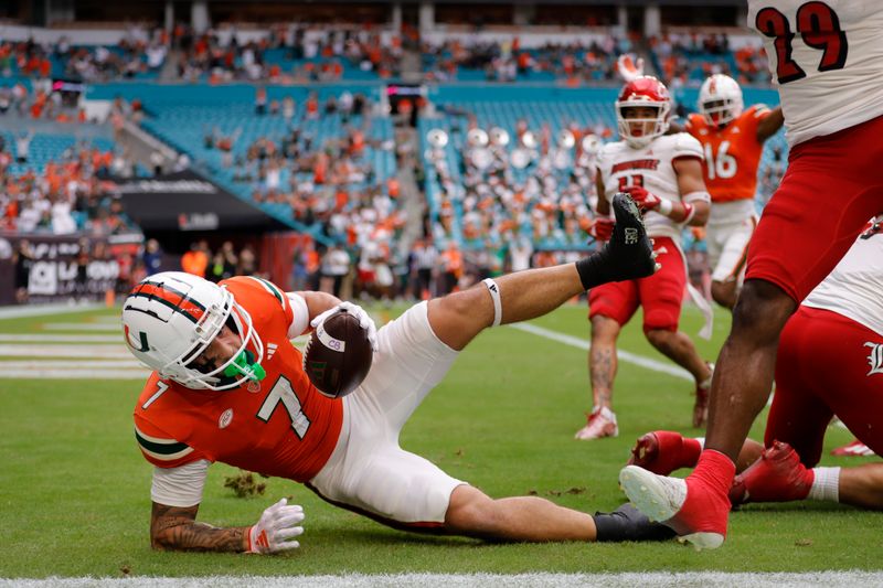 Nov 18, 2023; Miami Gardens, Florida, USA; Miami Hurricanes wide receiver Xavier Restrepo (7) leaps over Louisville Cardinals defensive lineman Mason Reiger (95) for a touchdown during the first quarter at Hard Rock Stadium. Mandatory Credit: Sam Navarro-USA TODAY Sports