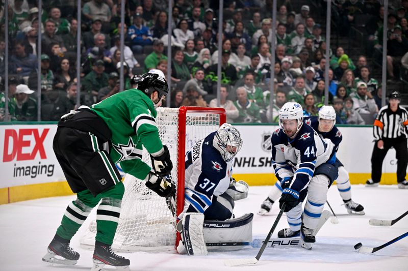 Apr 10, 2025; Dallas, Texas, USA; Dallas Stars left wing Jamie Benn (14) passes the puck by Winnipeg Jets goaltender Connor Hellebuyck (37) and defenseman Josh Morrissey (44) during the second period at the American Airlines Center. Mandatory Credit: Jerome Miron-Imagn Images