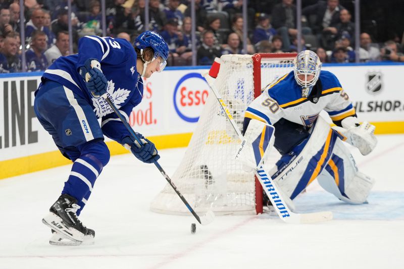 Oct 24, 2024; Toronto, Ontario, CAN; Toronto Maple Leafs forward Matthew Knies (23) tries to control the puck in front of St. Louis Blues goaltender Jordan Binnington (50) during the first period at Scotiabank Arena. Mandatory Credit: John E. Sokolowski-Imagn Images