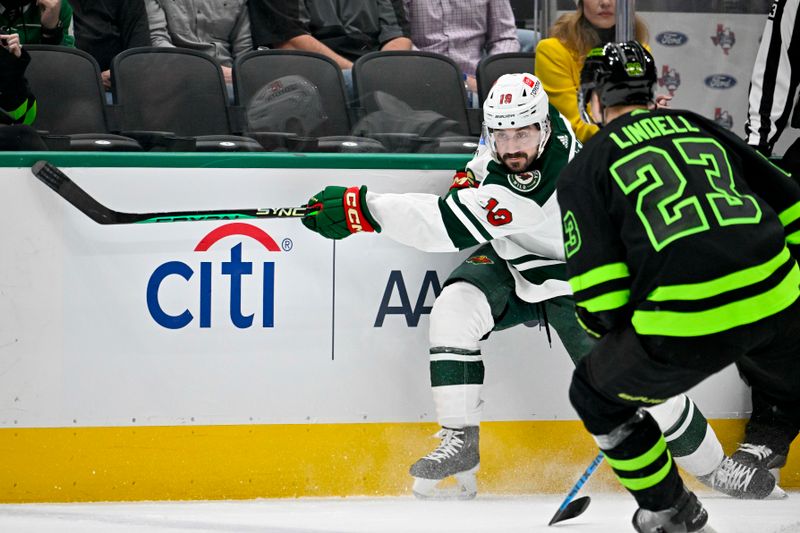 Jan 10, 2024; Dallas, Texas, USA; Minnesota Wild center Nic Petan (19) dumps the puck into the Stars zone in front of Dallas Stars defenseman Esa Lindell (23) during the first period at the American Airlines Center. Mandatory Credit: Jerome Miron-USA TODAY Sports