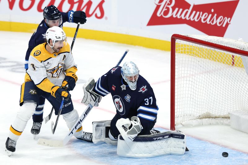 Oct 18, 2025; Winnipeg, Manitoba, CAN; Winnipeg Jets defenseman Neal Pionk (4), Nashville Predators left wing Filip Forsberg (9) and Winnipeg Jets goaltender Connor Hellebuyck (37) watch the puck slide through the crease in the third period at Canada Life Centre. Mandatory Credit: James Carey Lauder-Imagn Images