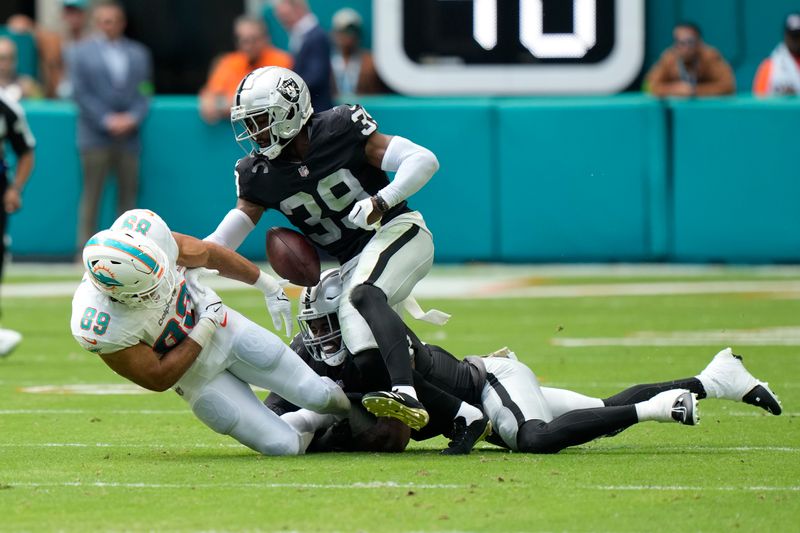 Miami Dolphins tight end Julian Hill (89) fumbles the ball under pressure from Las Vegas Raiders cornerback Nate Hobbs (39) and Divine Deablo during the first half of an NFL football game, Sunday, Nov. 19, 2023, in Miami Gardens, Fla. (AP Photo/Wilfredo Lee)