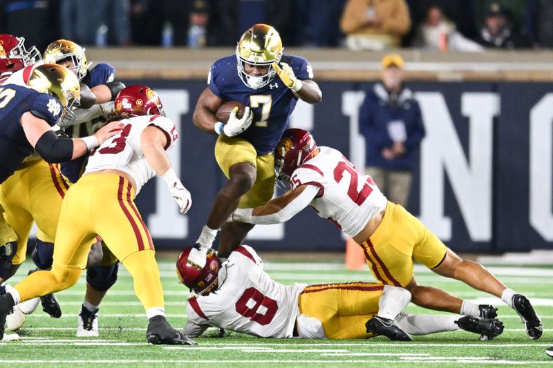 Oct 14, 2023; South Bend, Indiana, USA; Notre Dame Fighting Irish running back Audric Estime (7) jumps over USC Trojans safety Zion Branch (8) and linebacker Tackett Curtis (25) in the fourth quarter at Notre Dame Stadium. Mandatory Credit: Matt Cashore-USA TODAY Sports