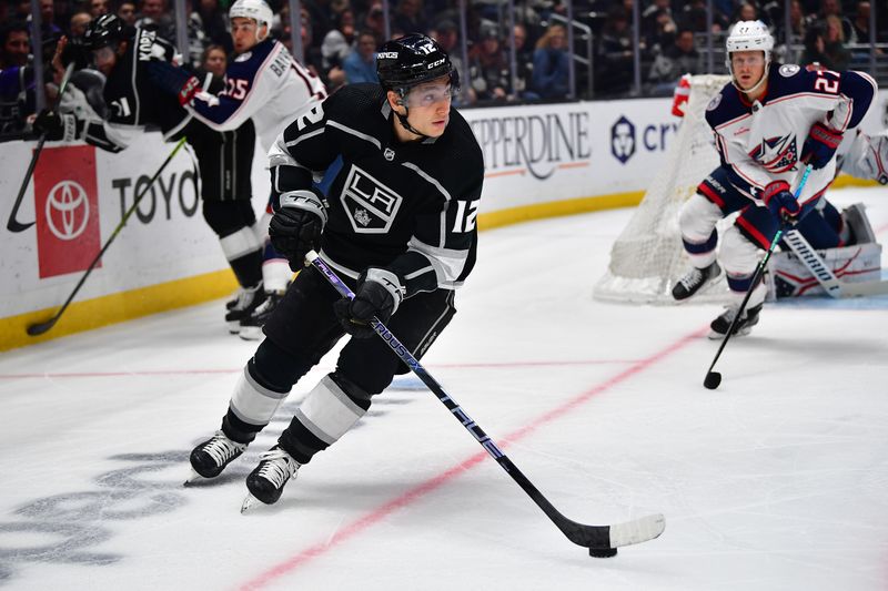 Mar 16, 2023; Los Angeles, California, USA; Los Angeles Kings left wing Trevor Moore (12) moves the puck ahead of Columbus Blue Jackets defenseman Adam Boqvist (27) during the second period at Crypto.com Arena. Mandatory Credit: Gary A. Vasquez-USA TODAY Sports