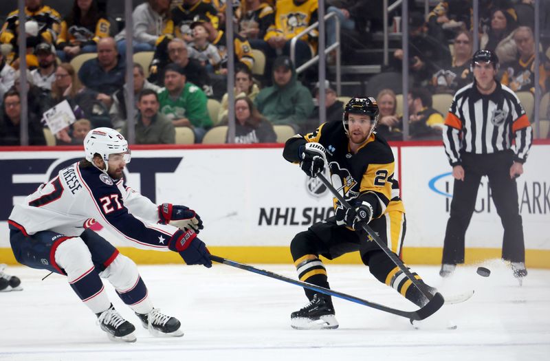 Mar 21, 2025; Pittsburgh, Pennsylvania, USA;  Pittsburgh Penguins defenseman Matt Grzelcyk (24) dumps the puck up ice past Columbus Blue Jackets center Zachary Aston-Reese (27) during the third period at PPG Paints Arena. Mandatory Credit: Charles LeClaire-Imagn Images
