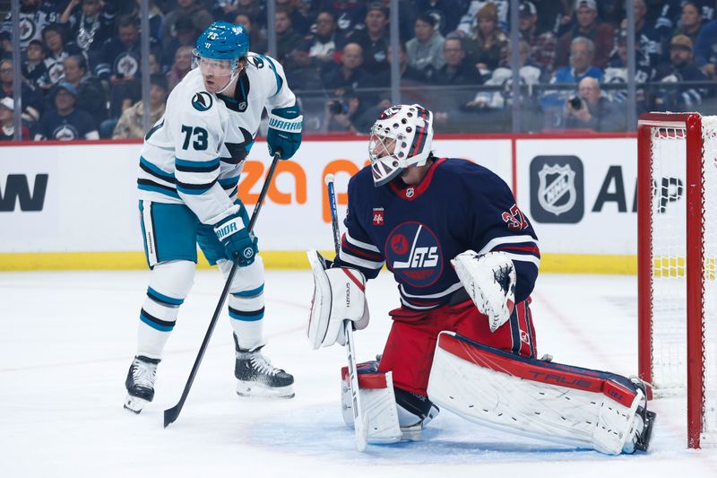 Oct 18, 2024; Winnipeg, Manitoba, CAN;  San Jose Sharks forward Tyler Toffoli (73) and Winnipeg Jets goalie Connor Hellebuyck (37) look for the puck during the first period at Canada Life Centre. Mandatory Credit: Terrence Lee-Imagn Images