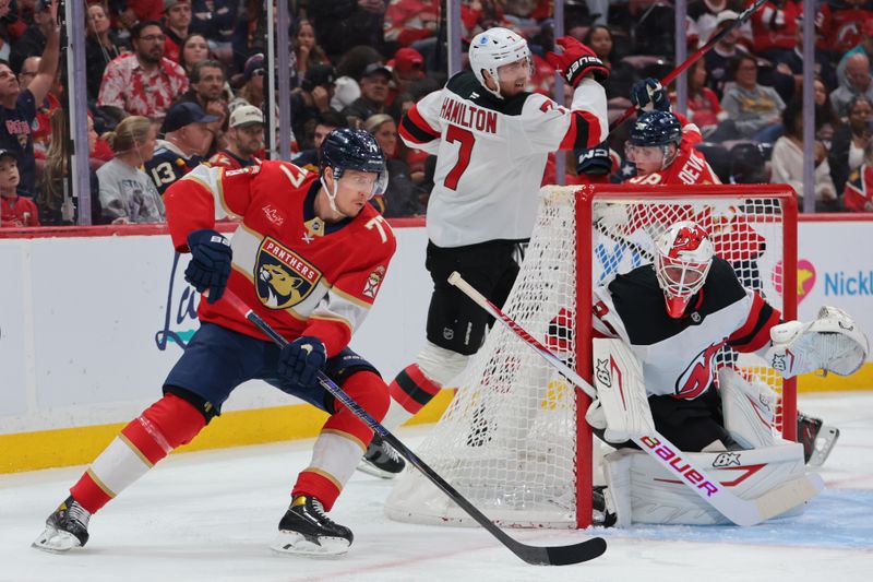 Nov 20, 2025; Sunrise, Florida, USA; Florida Panthers defenseman Niko Mikkola (77) moves the puck behind the net of New Jersey Devils goaltender Jake Allen (34) during the second period at Amerant Bank Arena. Mandatory Credit: Sam Navarro-Imagn Images