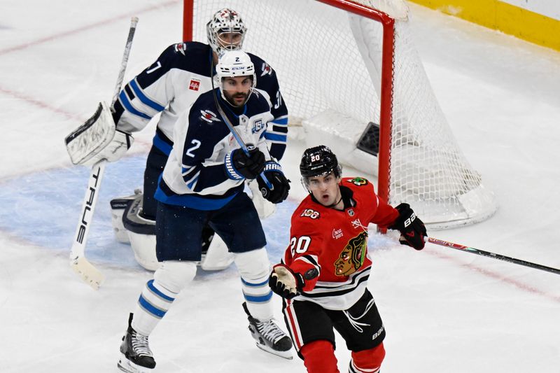 Jan 19, 2026; Chicago, Illinois, USA; Chicago Blackhawks center Ryan Greene (20) plays an errant puck with his glove against Winnipeg Jets defenseman Dylan DeMelo (2) and goaltender Connor Hellebuyck (37) during the second period at United Center. Mandatory Credit: Matt Marton-Imagn Images