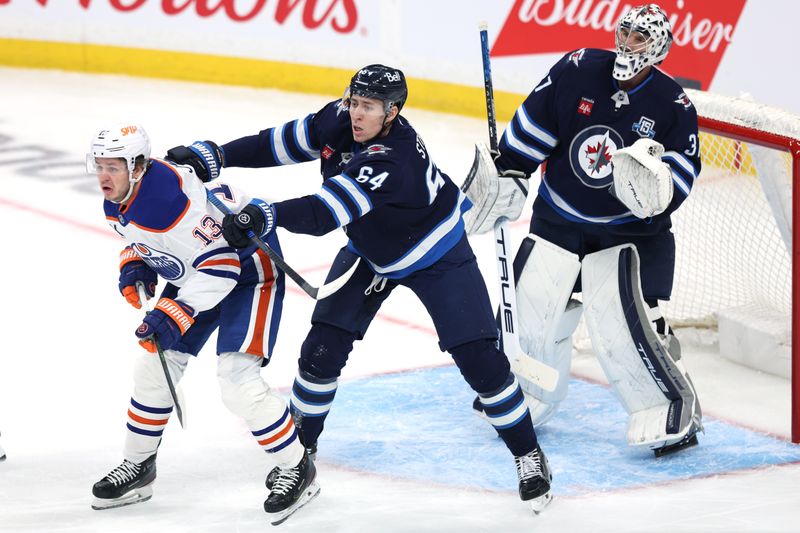 Dec 29, 2025; Winnipeg, Manitoba, CAN; Winnipeg Jets defenseman Logan Stanley (64) checks Edmonton Oilers center Mattias Janmark (13) in front of Winnipeg Jets goaltender Connor Hellebuyck (37) in the first period at Canada Life Centre. Mandatory Credit: James Carey Lauder-Imagn Images